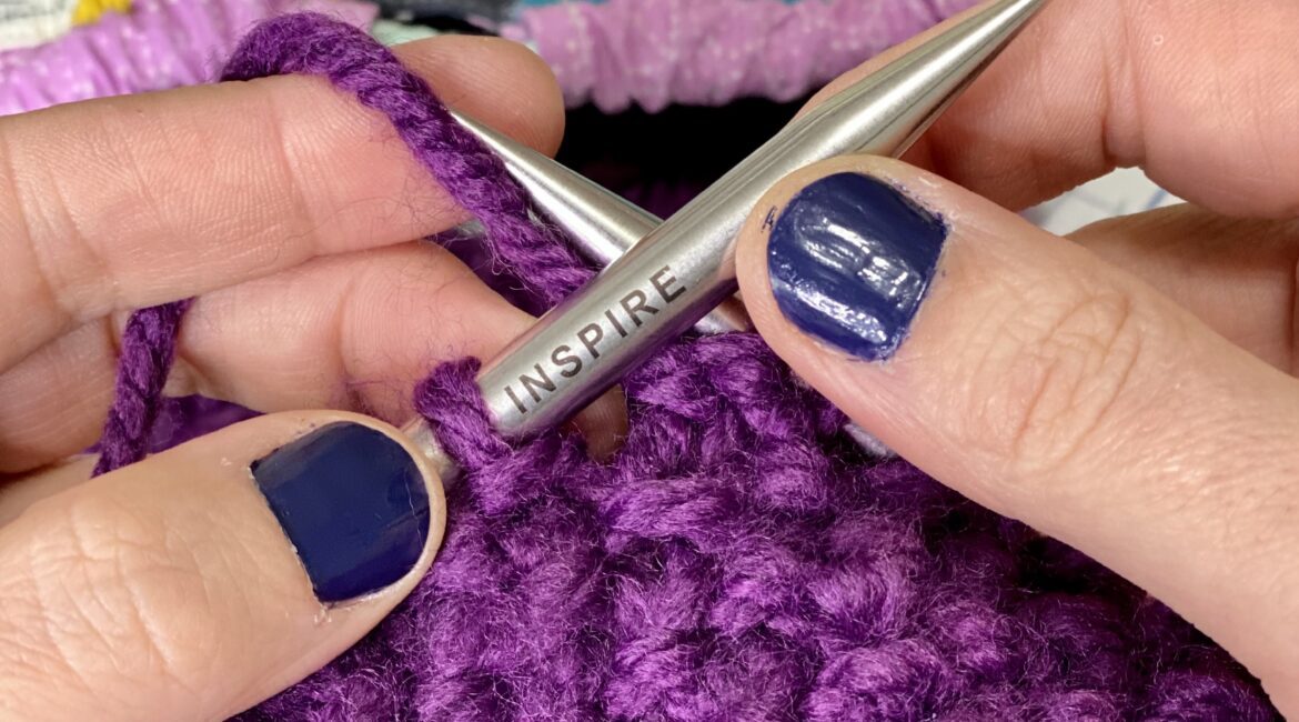 knitting a purple blanket with a pair of knitting needles